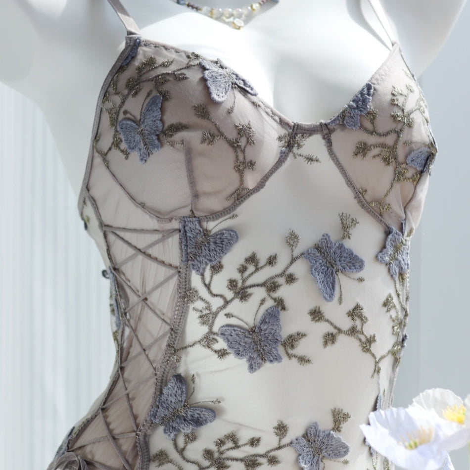 Sheer bodysuit with grey butterfly embroidery and floral lace detailing, featuring a lace-up side design on transparent mesh fabric, displayed on a mannequin.