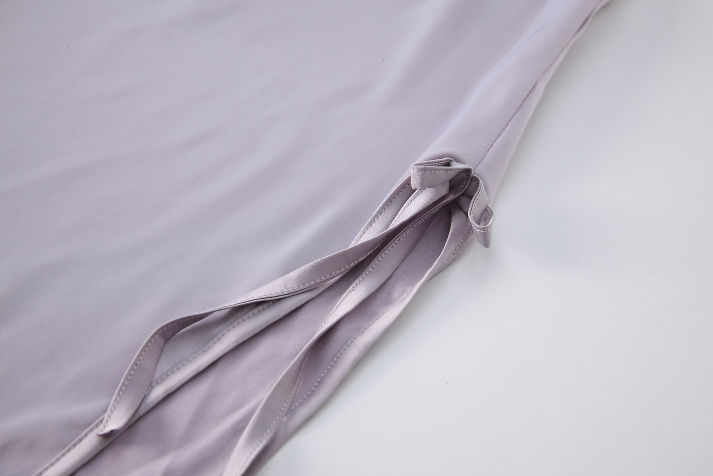 Close-up of the hem and ribbon details of a light purple silk nightgown, showcasing the elegant fabric and craftsmanship.