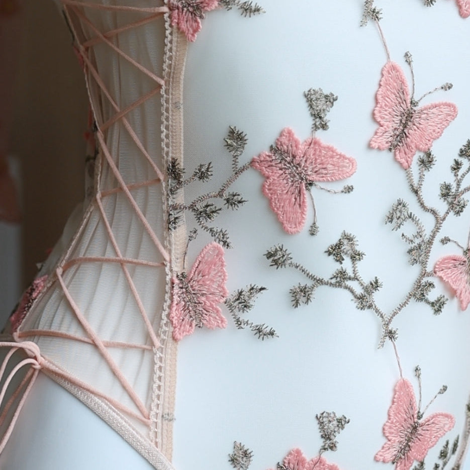 Close-up of a sheer bodysuit with pink butterfly embroidery and floral lace details, featuring a lace-up side design on transparent mesh fabric.