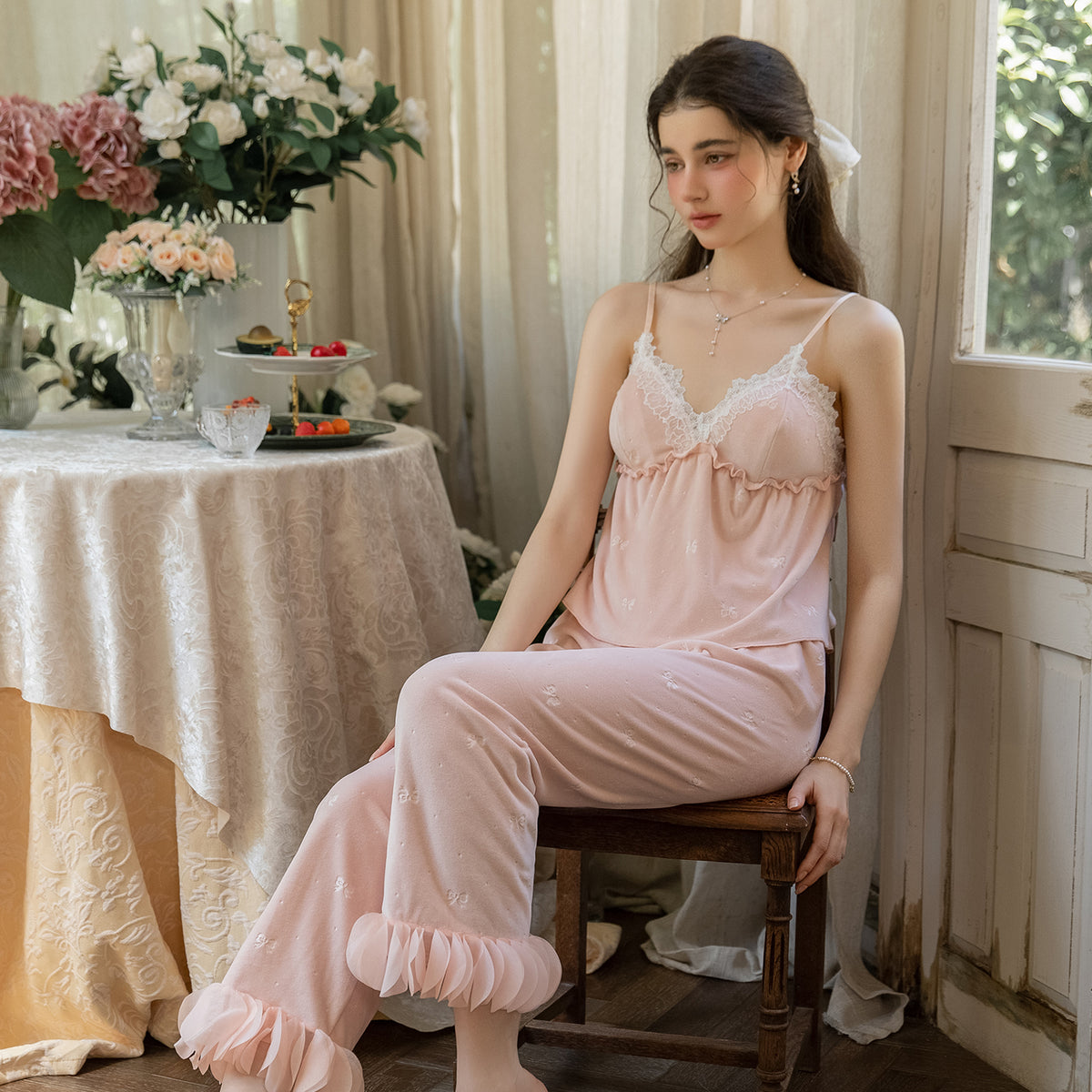 Seated model wearing the blush pink lace-trim camisole and ruffle-hem pajama pants